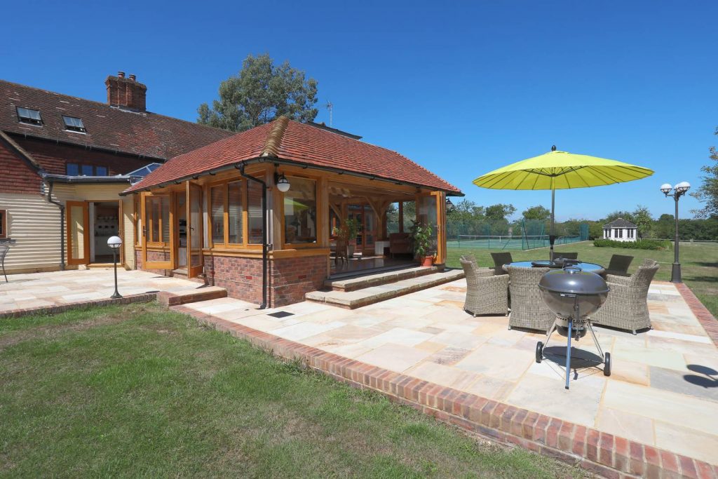 Timber frame house extension with a barbeque grill and garden furniture outside 