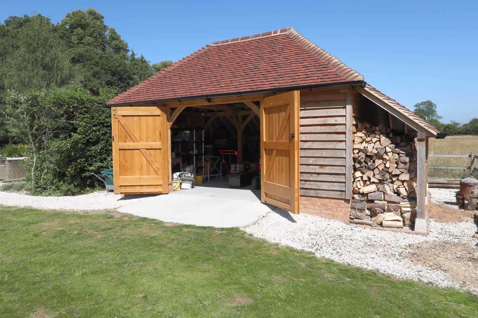 An oak framed single garage with the doors open and a wood store attached to the side